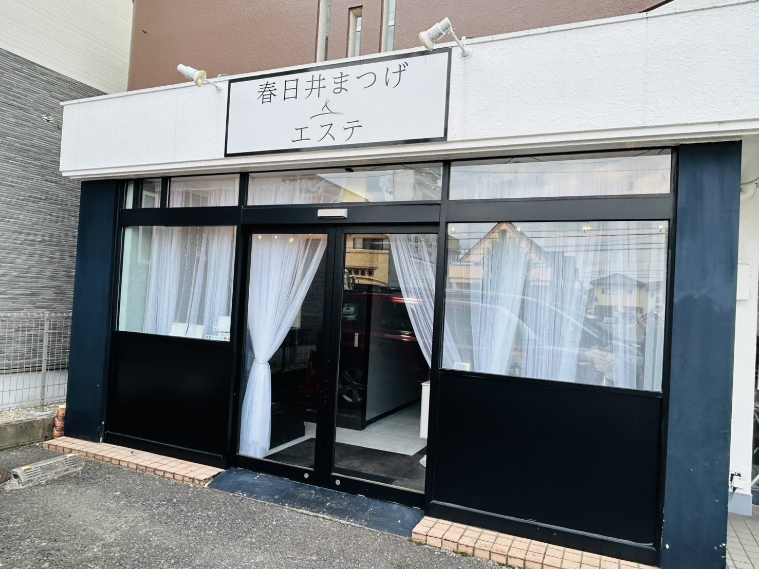 春日井まつげ＆エステの外観。黒い枠のガラス張りの入口と白い看板